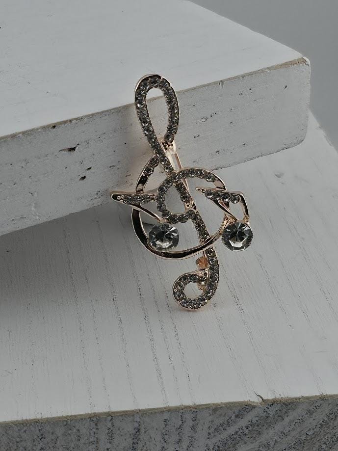 A close-up image of a decorative piece featuring a musical note motif, with a shiny gold-colored design and sparkling rhinestones or crystals.