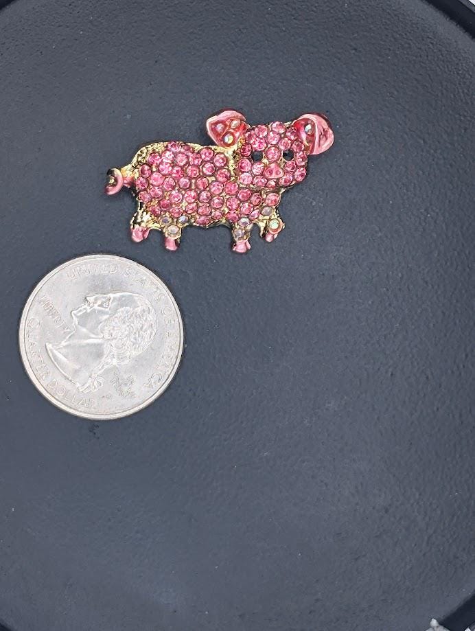 A pink rhinestone-encrusted brooch is placed next to a silver coin on a black surface.