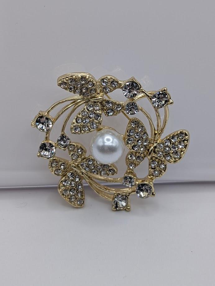 A decorative brooch with a white pearl at its center, surrounded by a floral design and sparkling crystal elements.