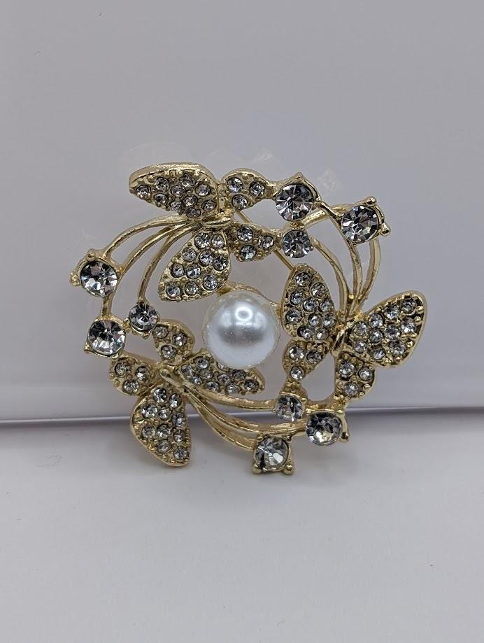 A decorative brooch with a white pearl at its center, surrounded by a floral design and sparkling crystal elements.