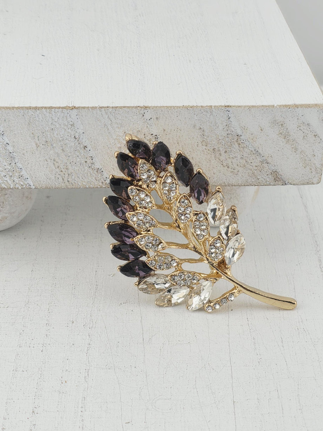 A decorative leaf-shaped brooch with a gold frame and sparkling crystal elements.