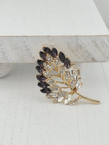 A decorative leaf-shaped brooch with a gold frame and sparkling crystal elements.