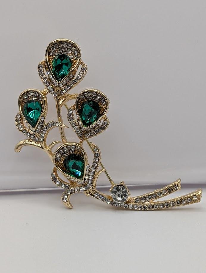 A decorative brooch with a branch-like design, featuring green gemstones and sparkling rhinestones.
