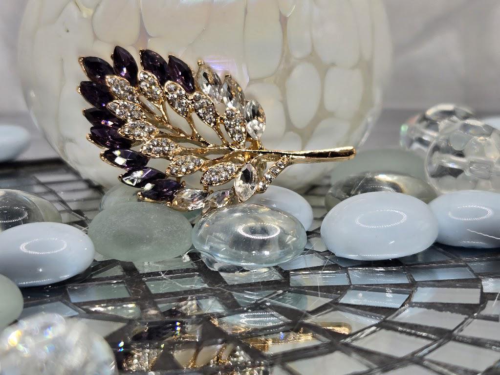 a decorative piece with a leaf-shaped design, adorned with sparkling gemstones, placed on a mosaic surface with small white and blue stones.