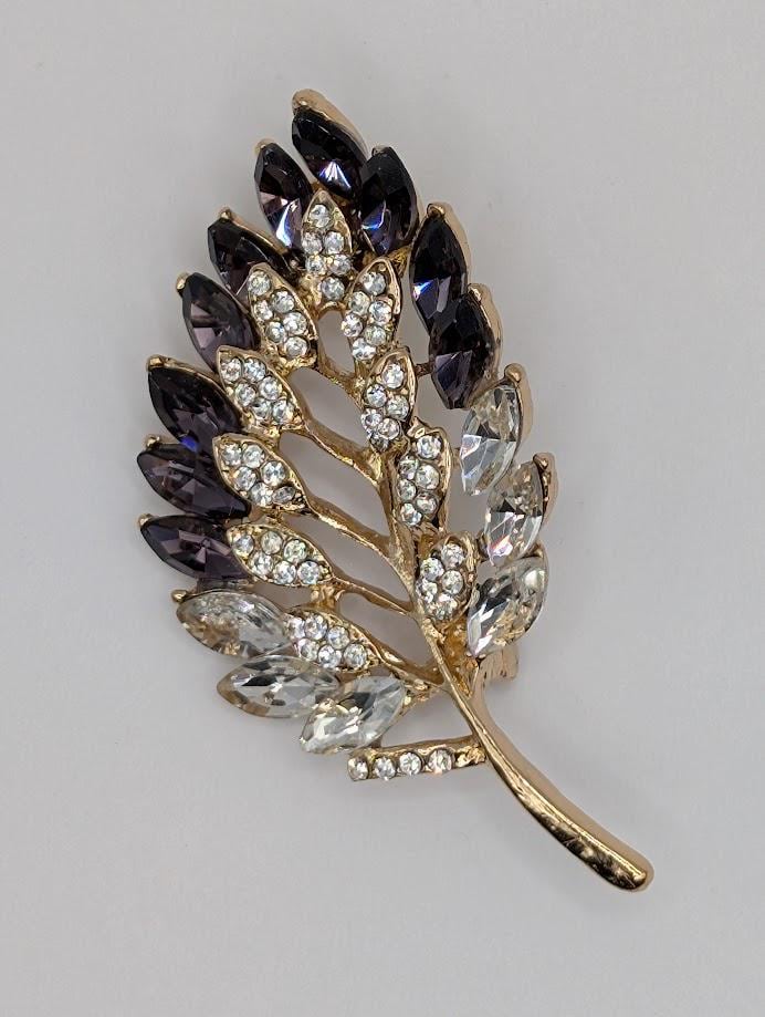 A decorative brooch in the shape of a leaf, adorned with numerous small diamonds.