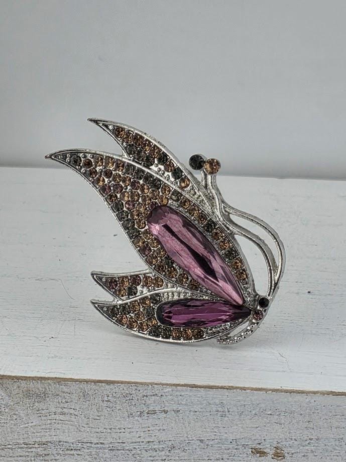 A silver butterfly brooch with a purple gemstone on its wing.