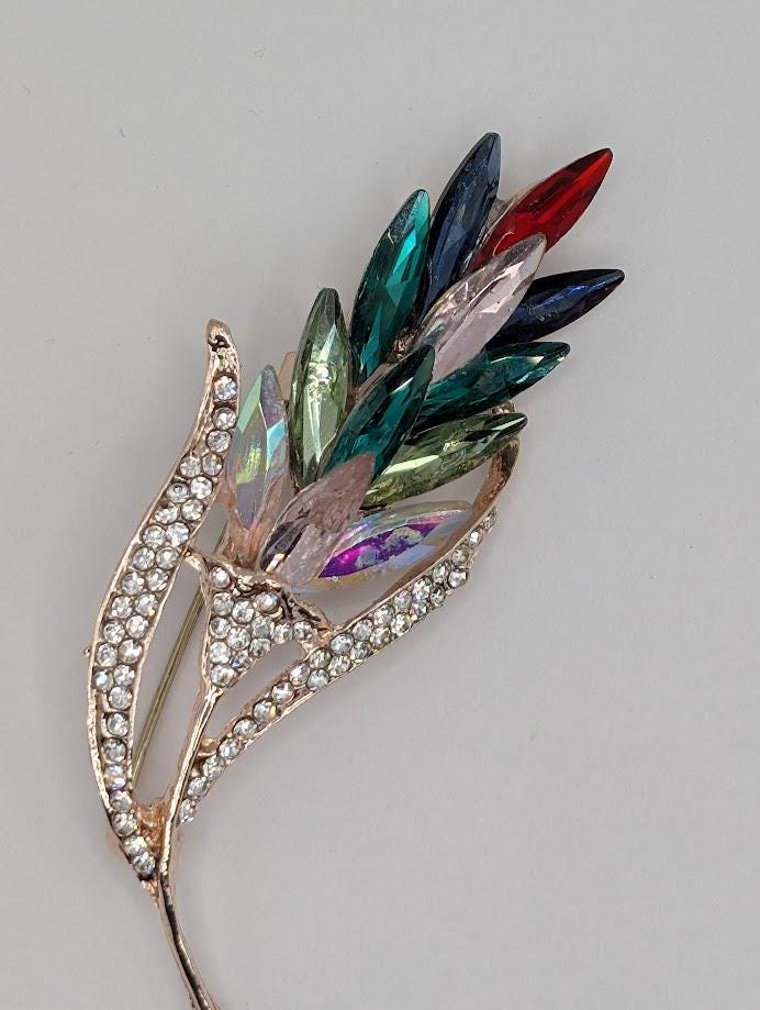 A decorative brooch with a leaf-like design and a variety of colorful gemstones.