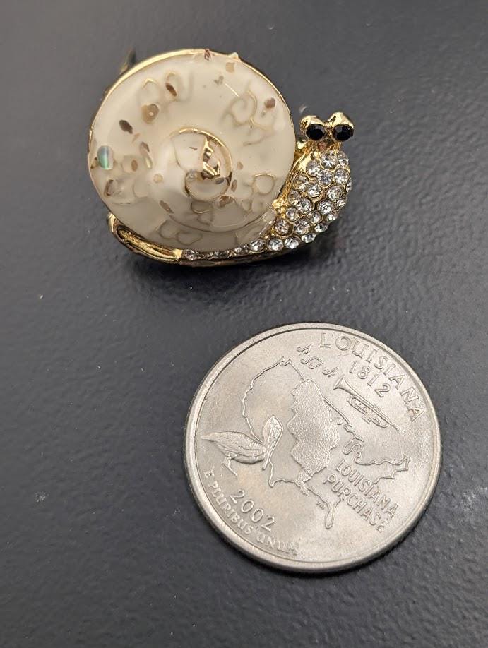 a decorative piece resembling a snail, which is placed next to a United States quarter.