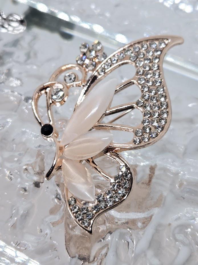 A close-up image of a decorative butterfly brooch with a combination of white and silver elements, including a large white wing with a black spot and small silver accents.