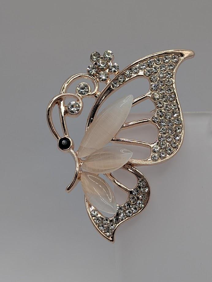 A decorative butterfly brooch with a gold-colored metal frame and a white and black design, adorned with small diamonds.