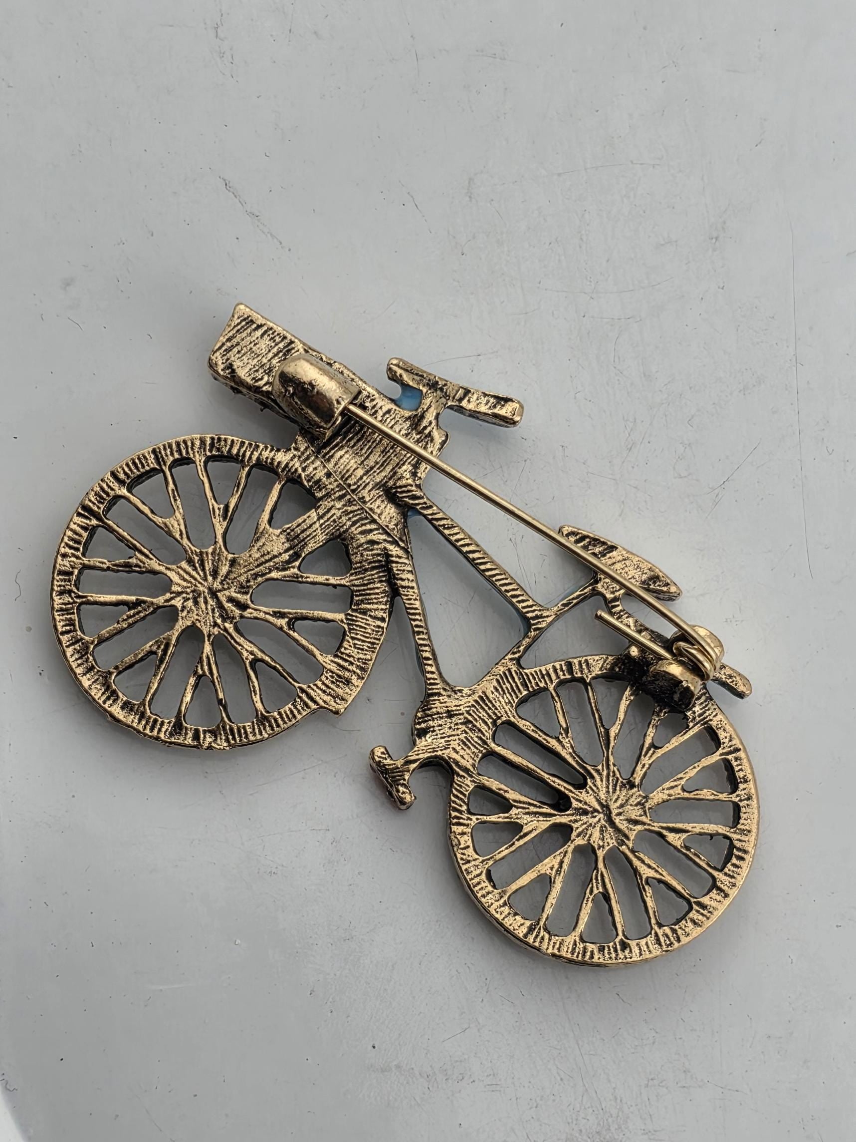 A close-up image of a small, intricately designed metal bicycle brooch or pin.