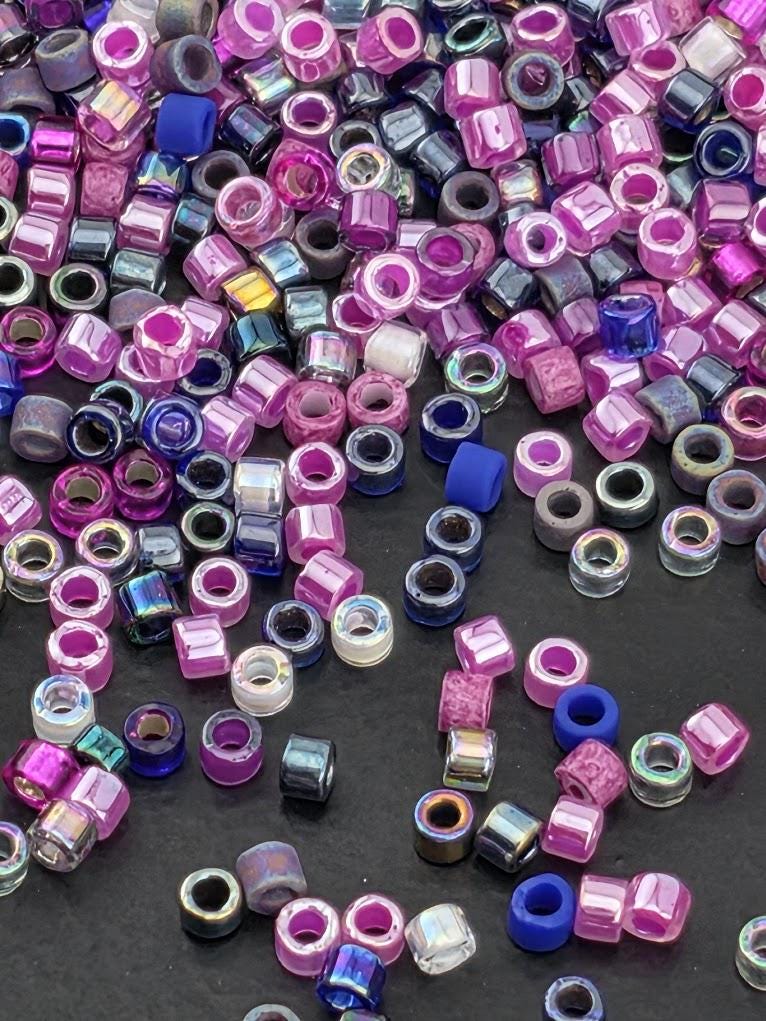 A colorful pile of multicolored beads, including shades of pink, purple, blue, and black, scattered across a surface.