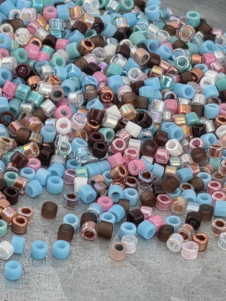 A colorful pile of various colored beads, including blue, pink, brown, and clear beads, scattered on a surface.