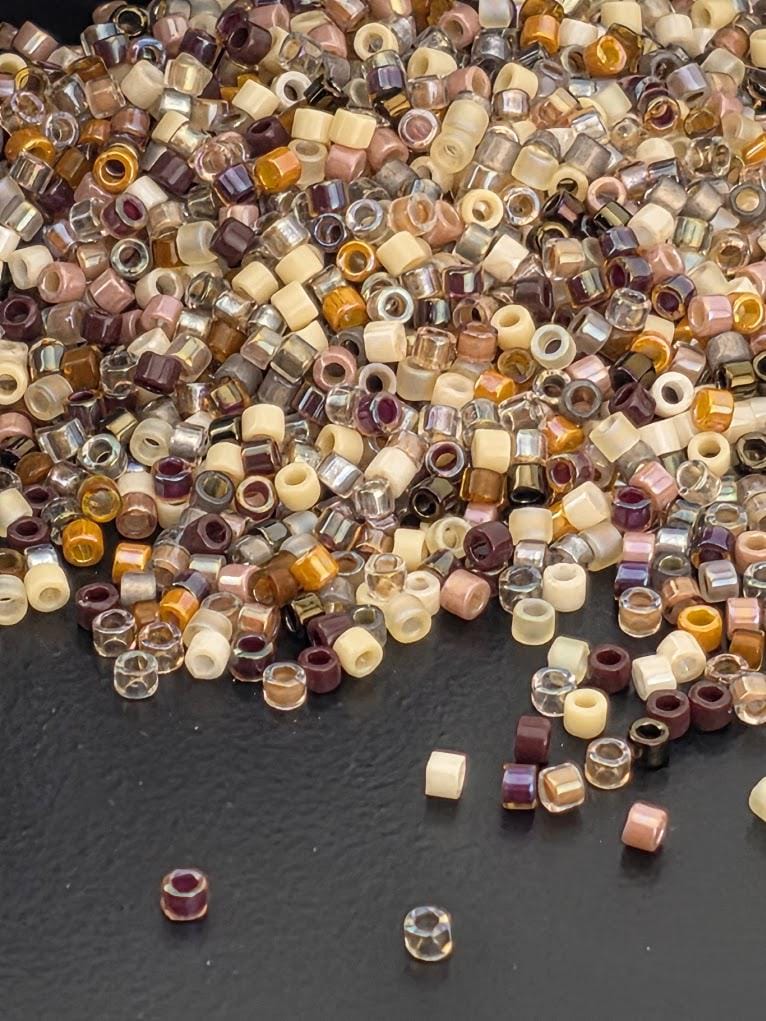 A large pile of multicolored beads, including various shades of brown, beige, and other colors, scattered across a white surface.