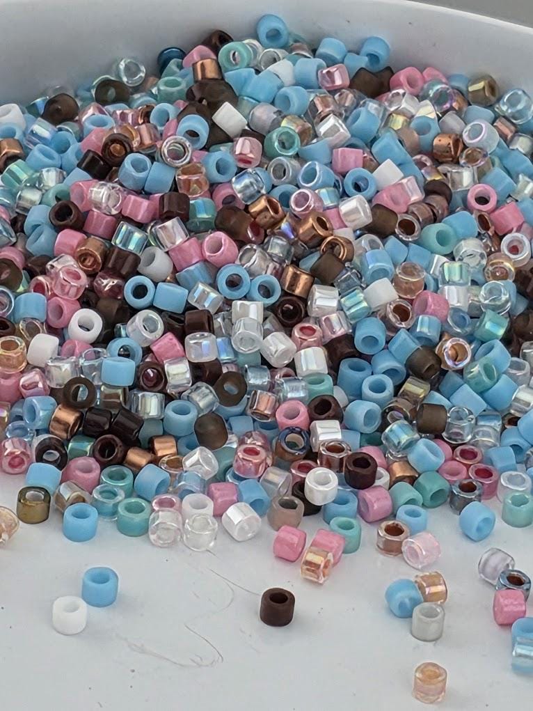 A pile of multicolored beads, including clear, blue, pink, brown, and multicolored beads, scattered on a surface.