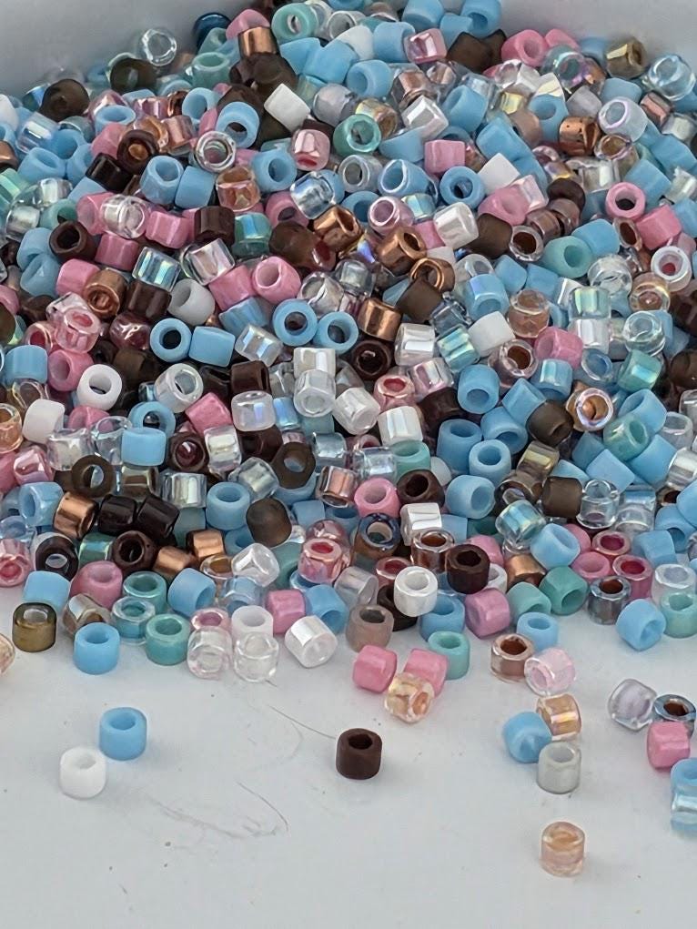 A pile of multicolored beads, including various shades of blue, pink, and brown, scattered on a white surface.