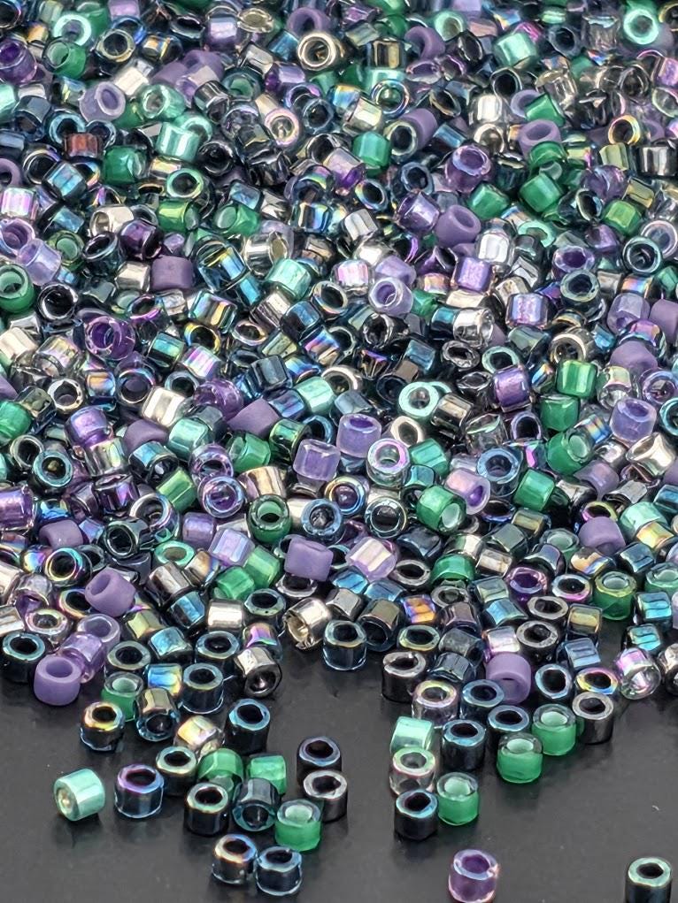 The image is a close-up of a pile of multicolored beads, including various shades of purple, green, blue, and silver. The beads are scattered across a dark surface, creating a visually striking and vibrant display.