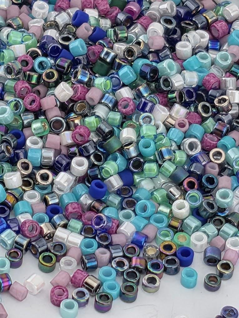A colorful assortment of multicolored beads, including various shades of blue, green, purple, and pink, scattered across a surface.