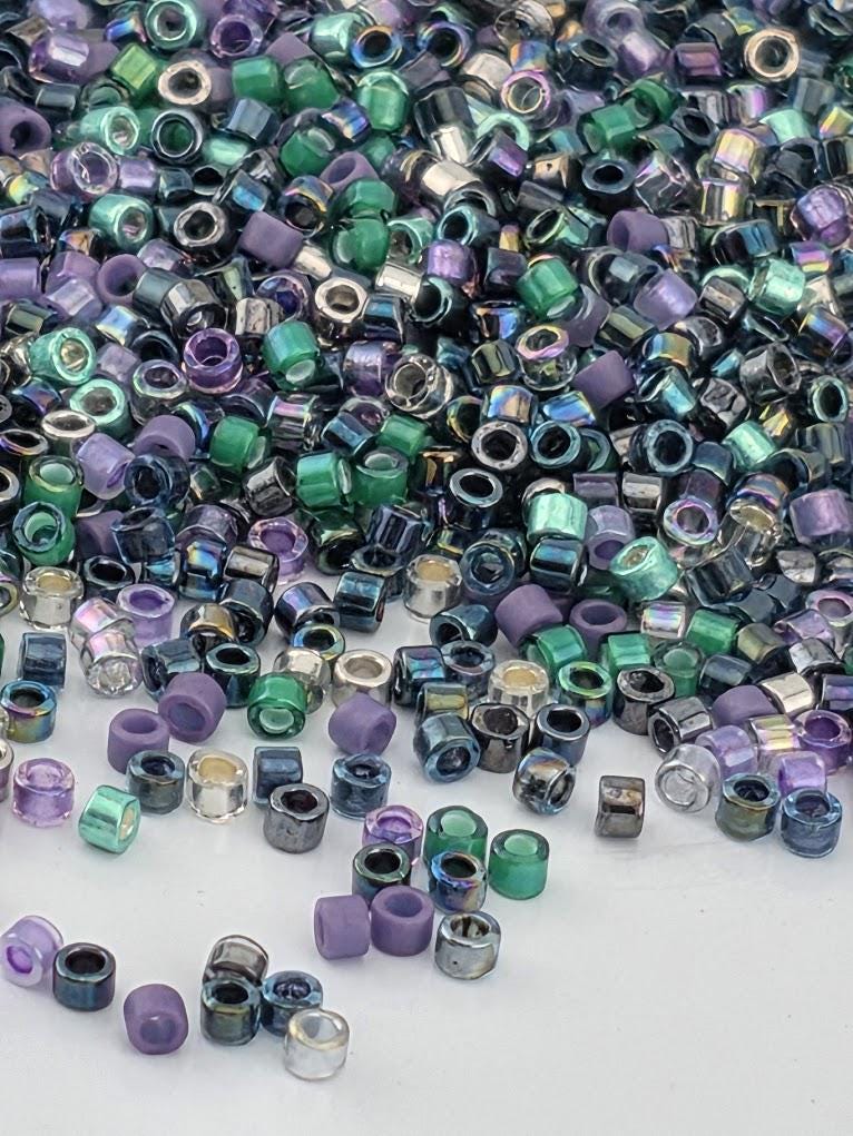 The image is a close-up of a pile of multicolored beads, including various shades of purple, green, blue, and silver. The beads are scattered across a dark surface, creating a visually striking and vibrant display.