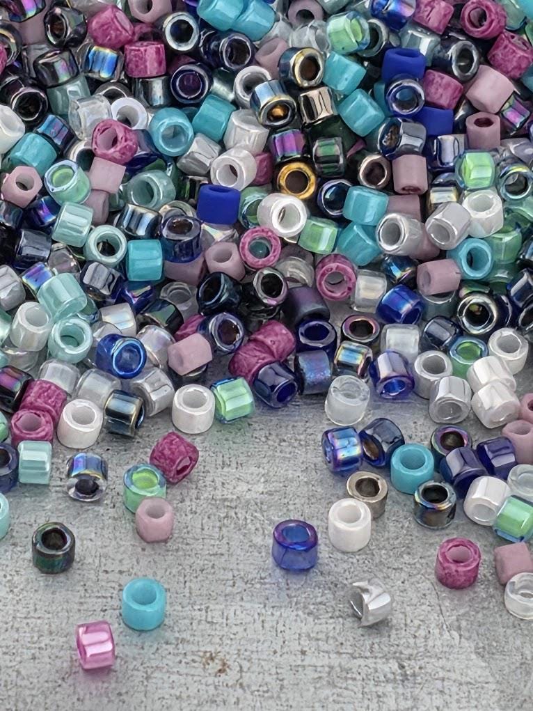 A colorful assortment of multicolored beads, including various shades of blue, green, purple, and pink, scattered across a surface.