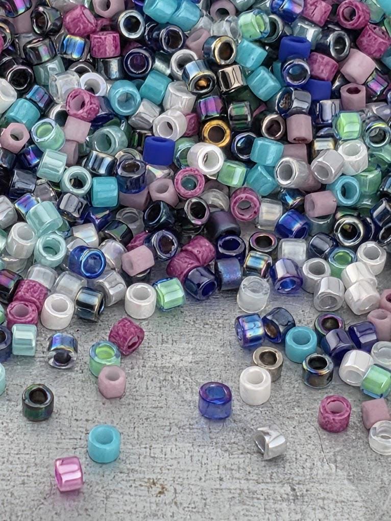 A colorful pile of multicolored beads, including various shades of blue, pink, purple, and white, scattered on a textured surface.