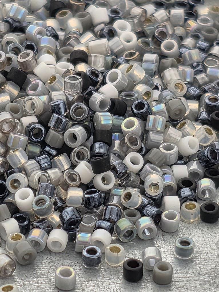 a large pile of various colored beads, including black, white, and silver, scattered on a dark surface.