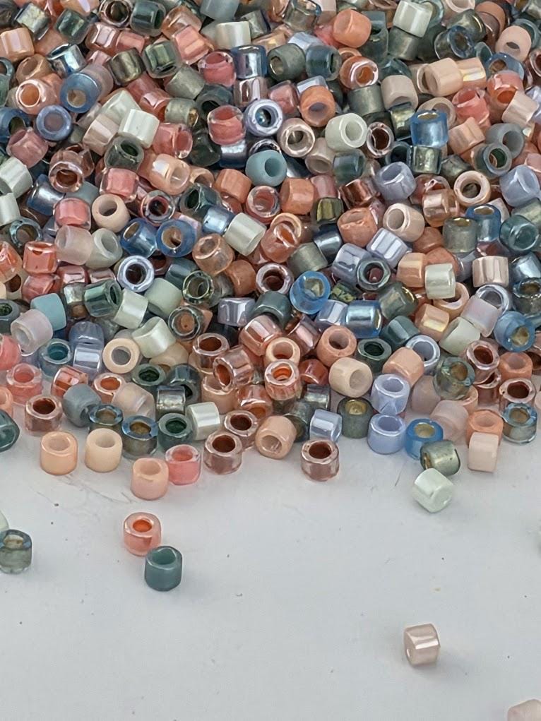 A pile of multicolored beads, including various shades of blue, pink, green, and orange, scattered on a white surface.