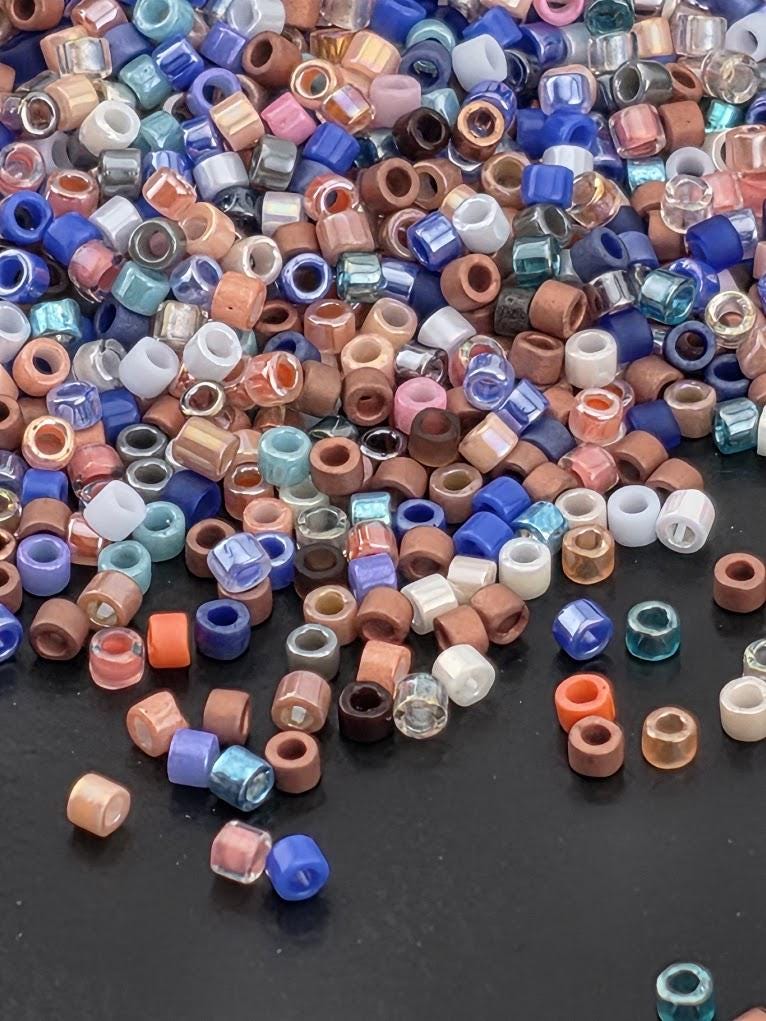 A pile of multicolored beads, including various shades of blue, pink, orange, and brown, scattered on a dark surface.