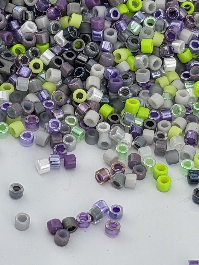 a large pile of multicolored beads, including various shades of purple, green, and gray, scattered across a surface.