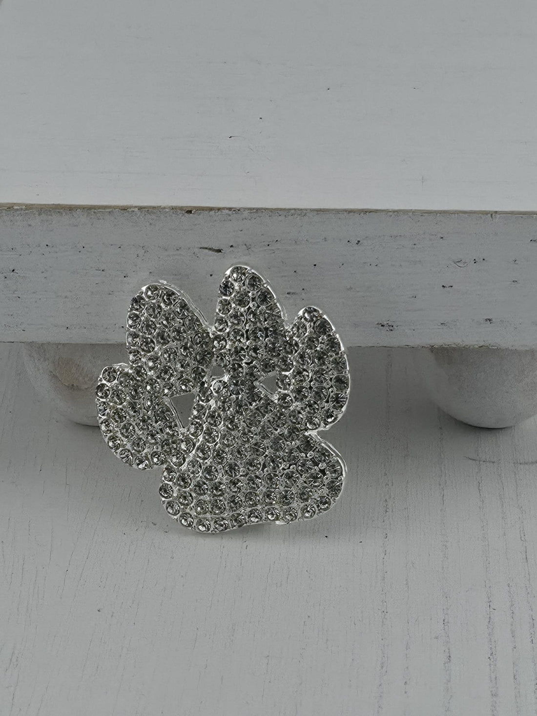 A silver decorative piece with a floral pattern and sparkling crystal elements is displayed against a white wooden background.