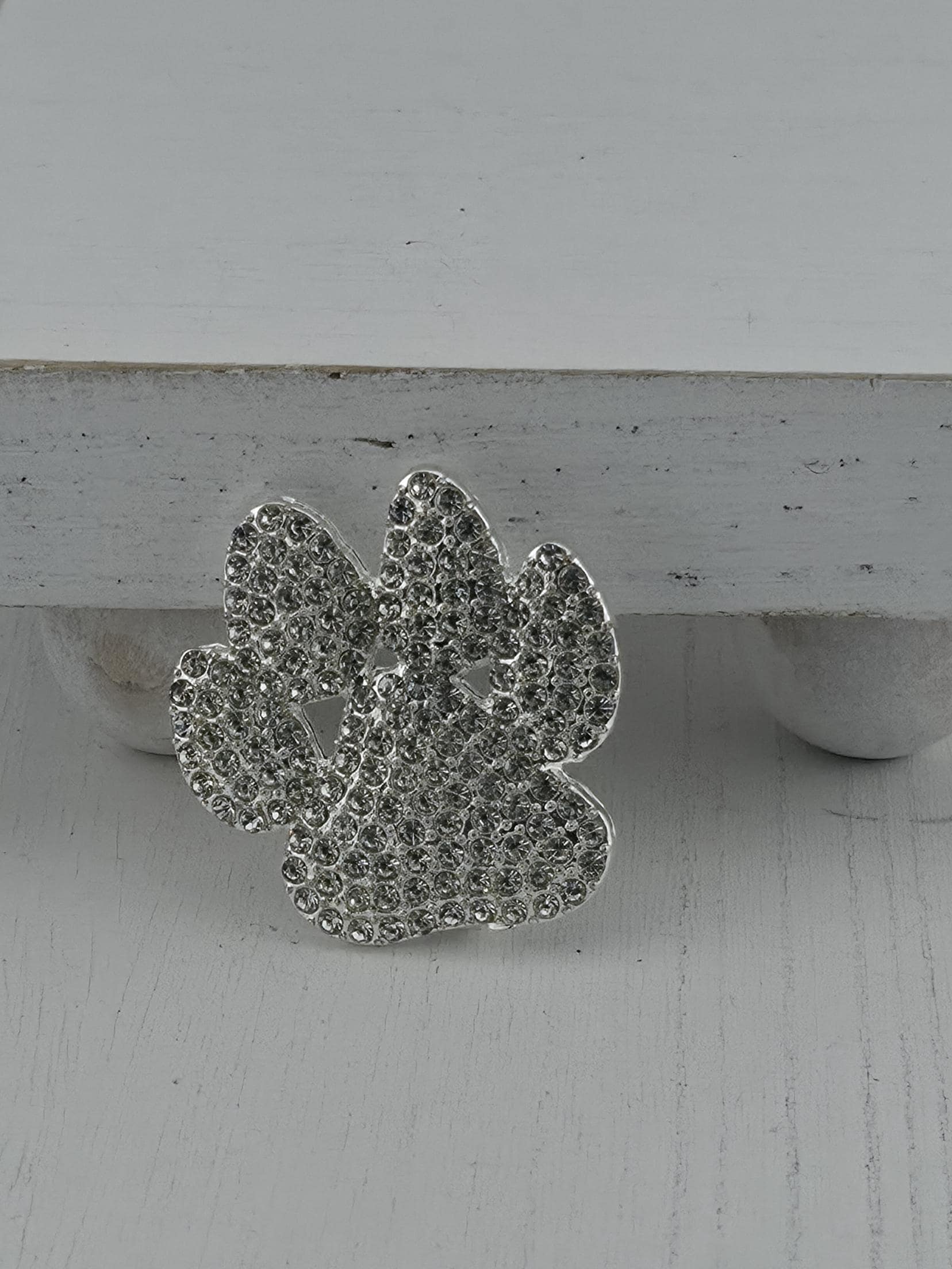 A silver decorative piece with a floral pattern and sparkling crystal elements is displayed against a white wooden background.