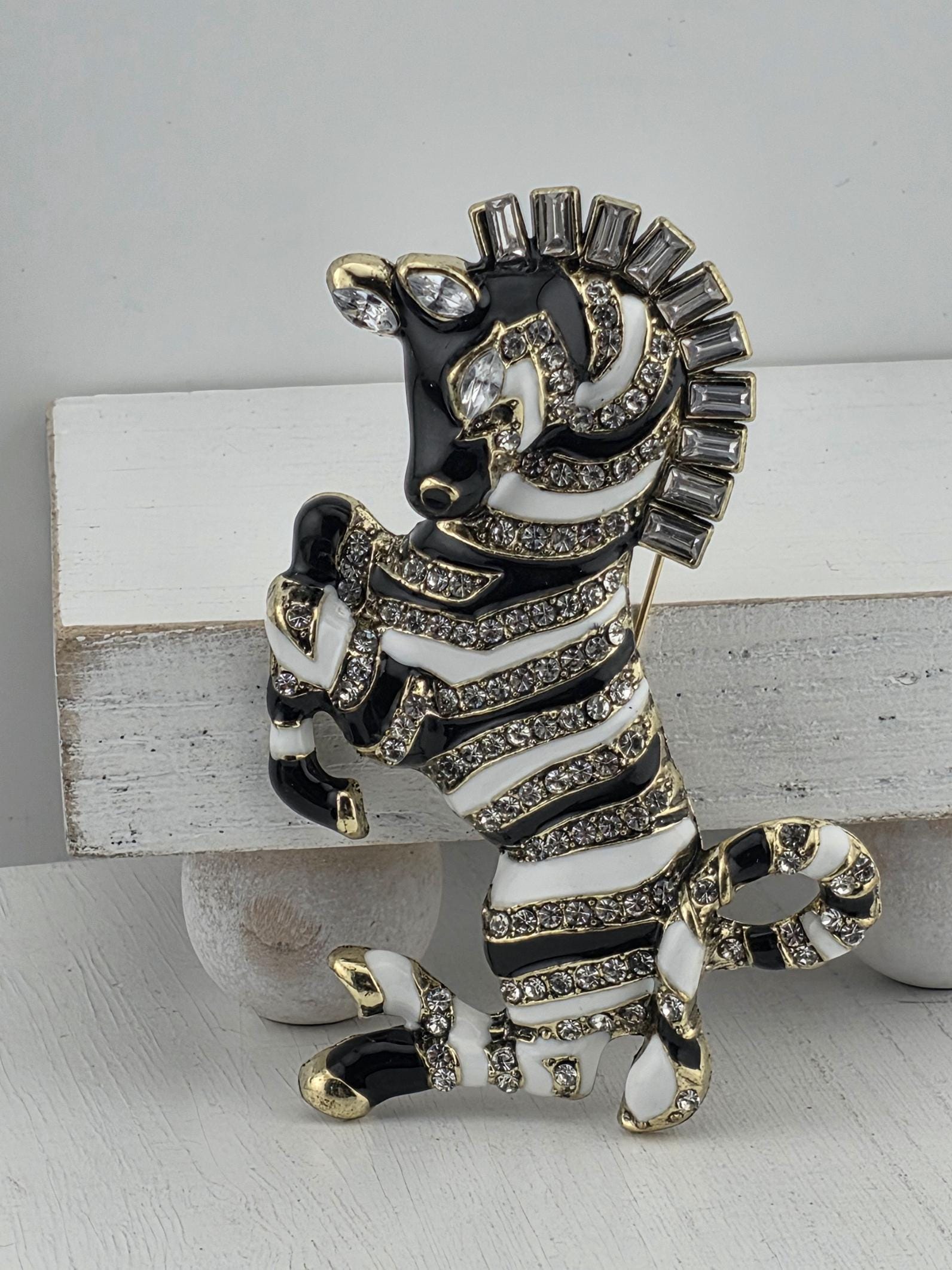 A decorative zebra brooch with black and white stripes, gold accents, and rhinestones or crystals.