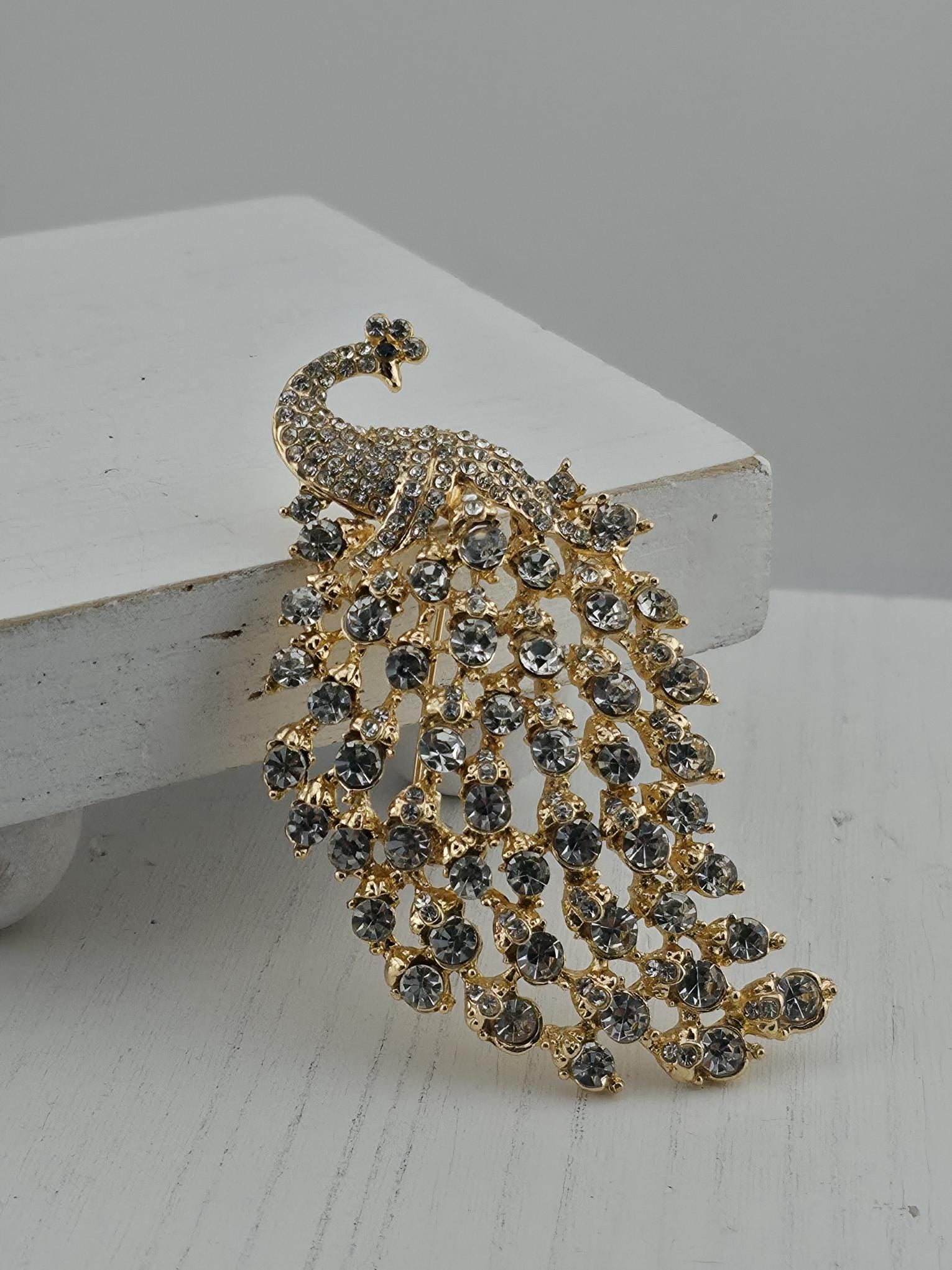 A decorative brooch in the shape of a peacock, adorned with numerous small, clear gemstones.