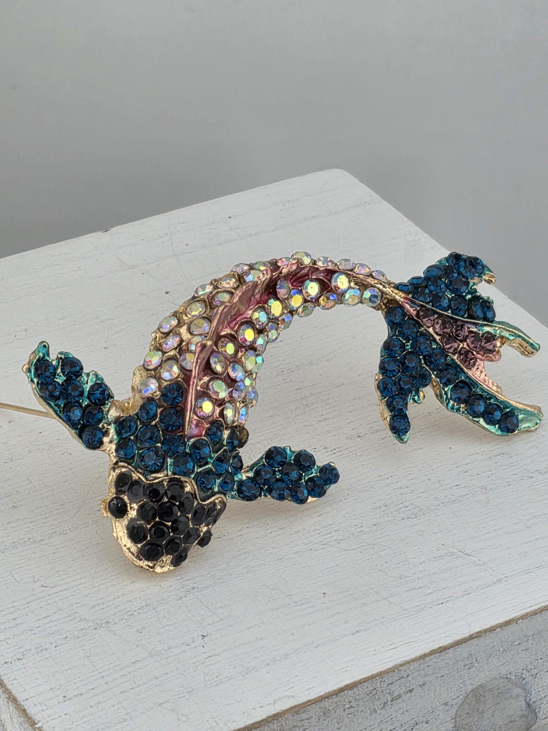 A decorative fish brooch with a colorful, sparkling design made of various materials, including gemstones and metal.