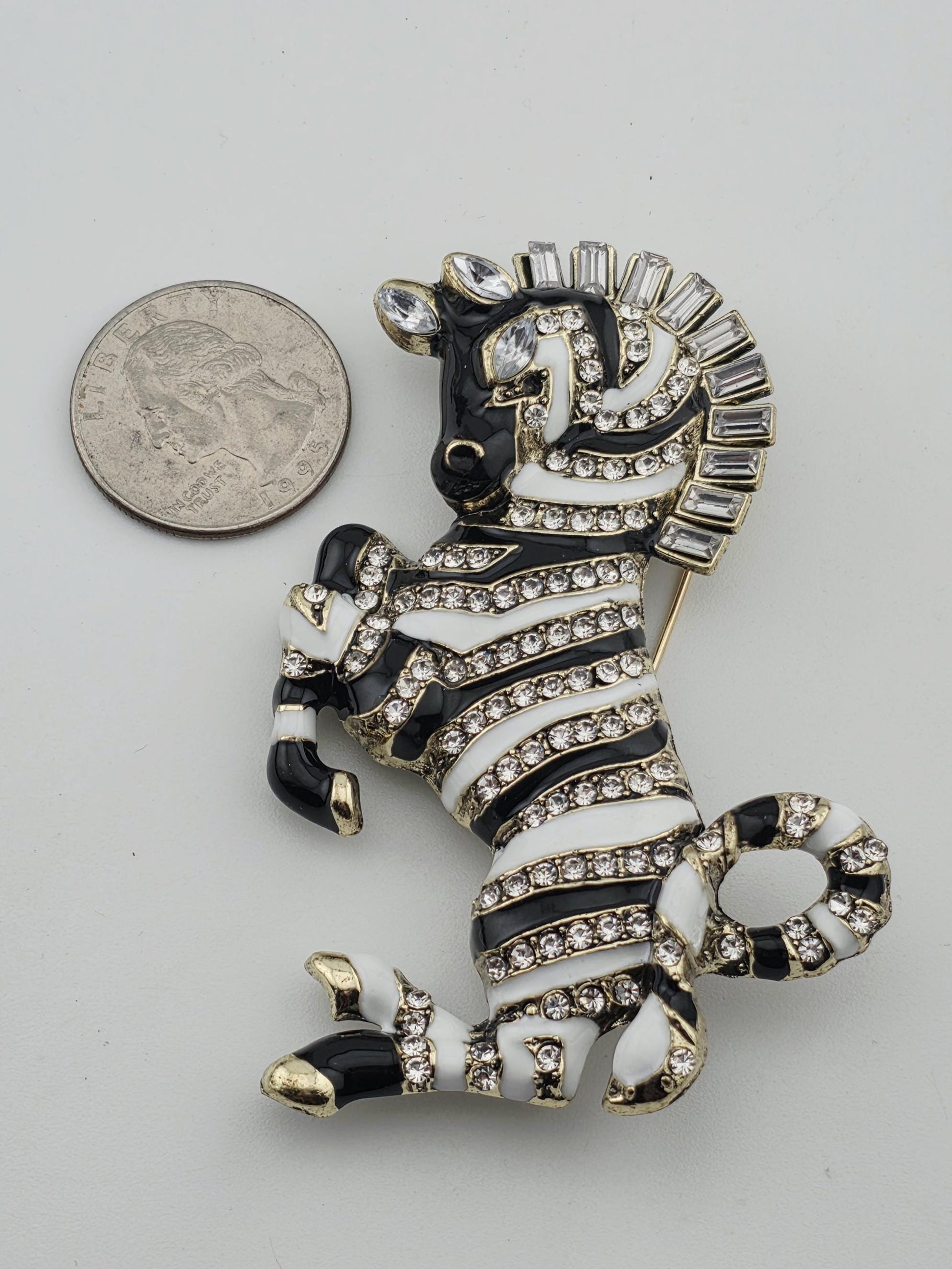 A decorative zebra brooch with rhinestones and a coin for scale.