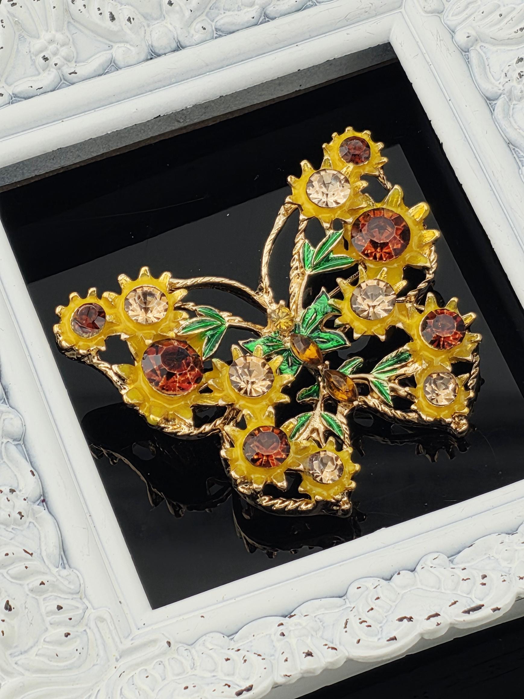 A decorative butterfly-shaped brooch with yellow and red gemstones, placed within a white ornate frame.