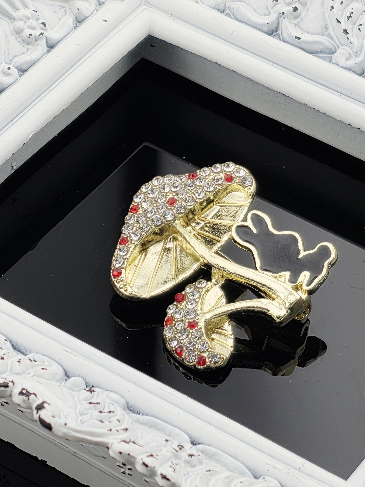 A decorative gold and diamond-encrusted brooch is displayed in a white ornate frame.