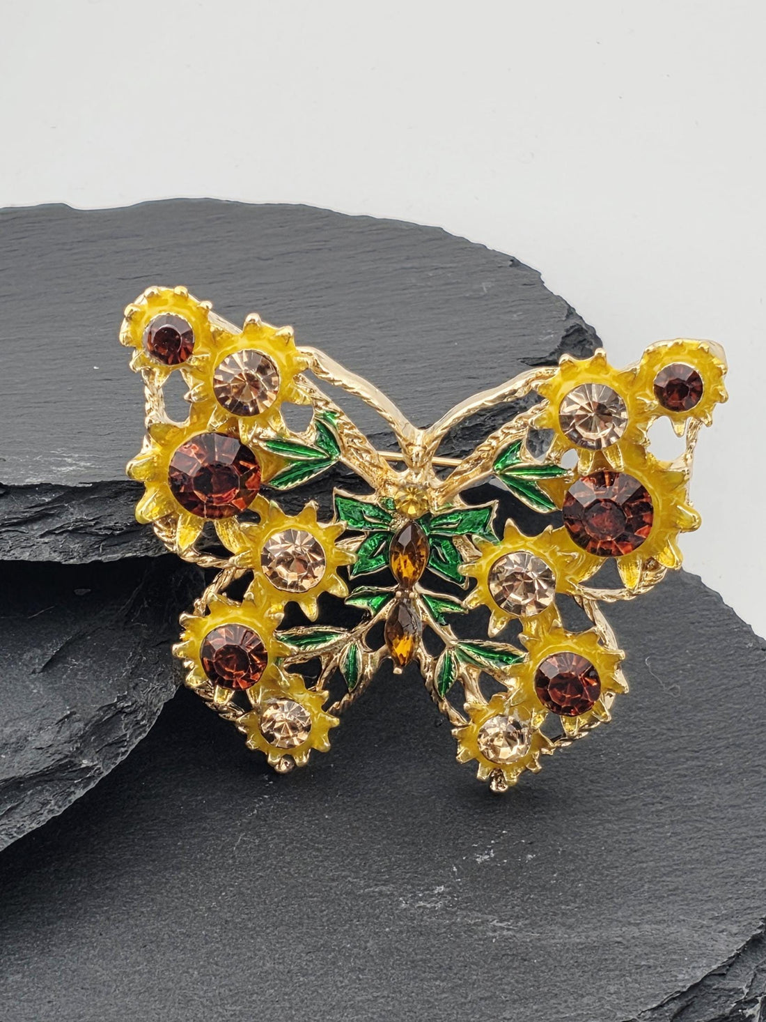 A decorative butterfly-shaped brooch with yellow and red gemstones, placed within a white ornate frame.