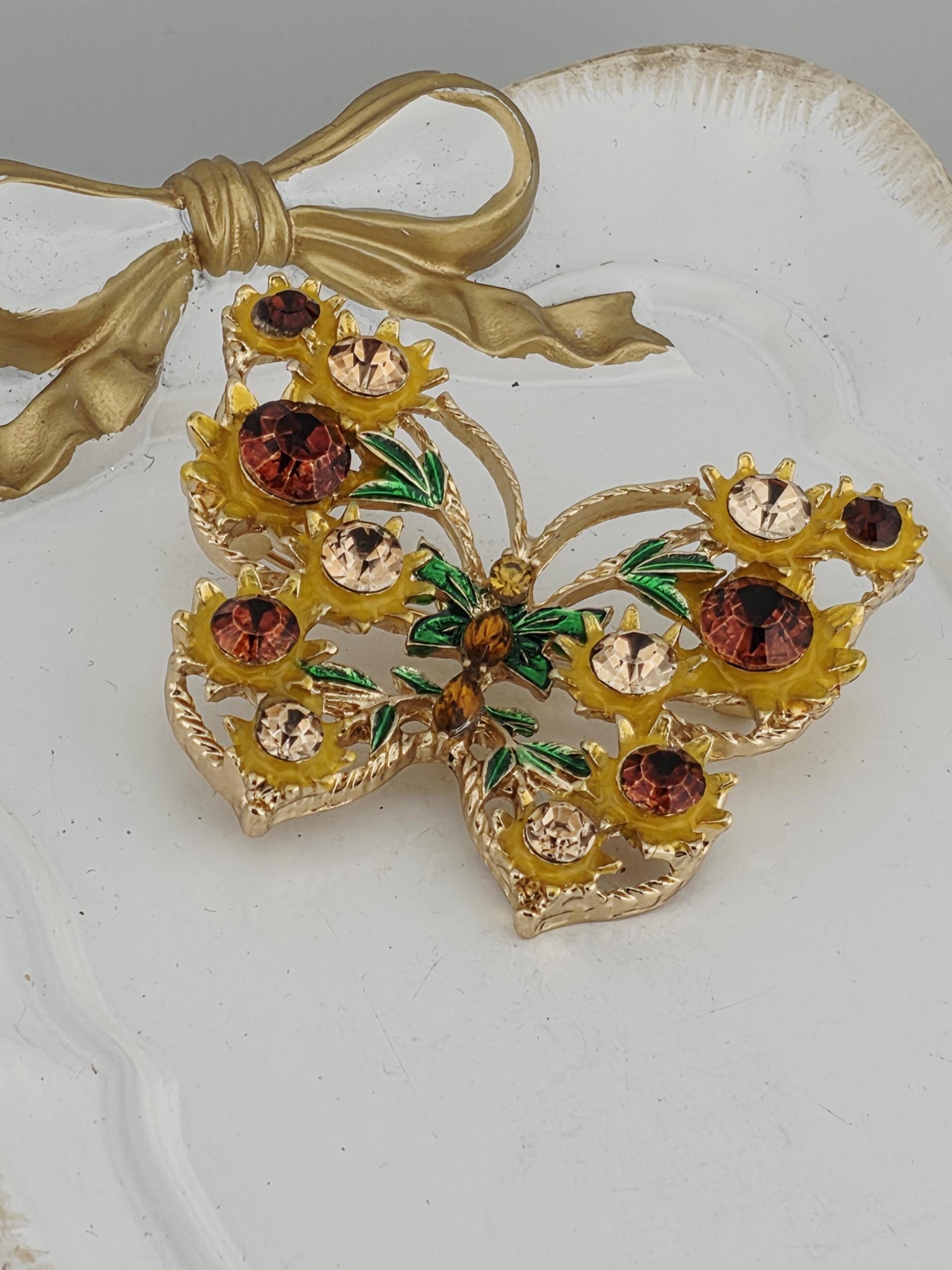 A decorative brooch with a floral design and colorful gemstones, including yellow, red, and brown stones, is displayed against a white background.