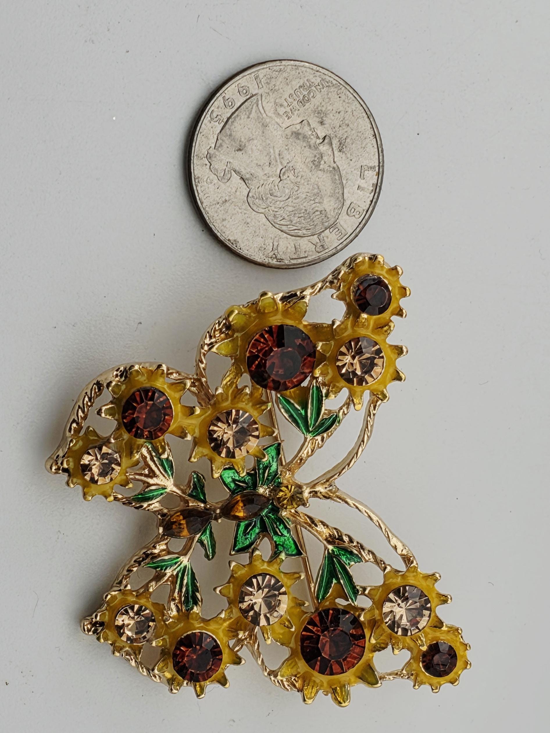 A butterfly brooch adorned with yellow flowers and brown gemstones is placed next to a United States quarter coin.