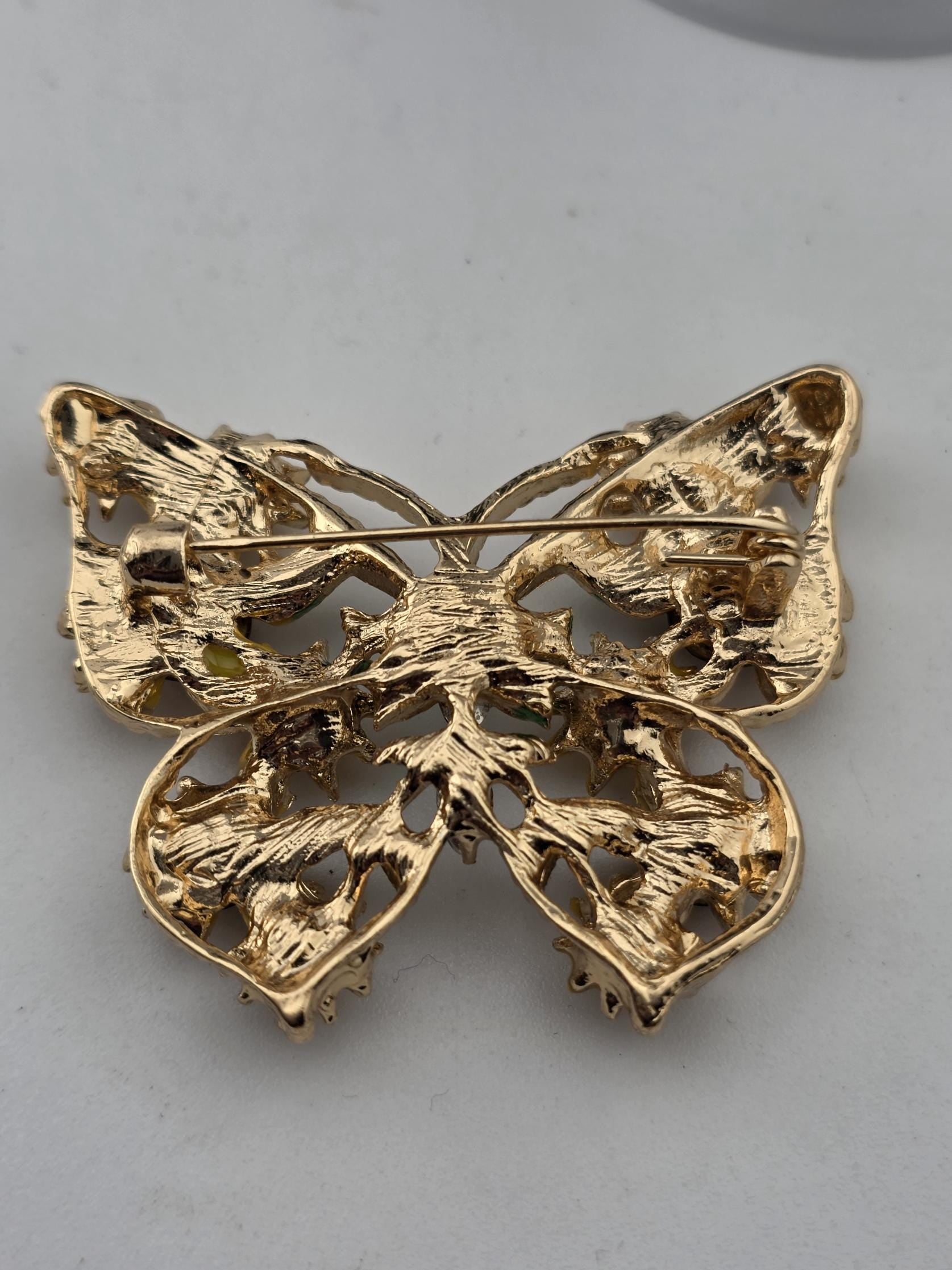 A gold-colored pin in the shape of a butterfly, with intricate details and a textured surface.