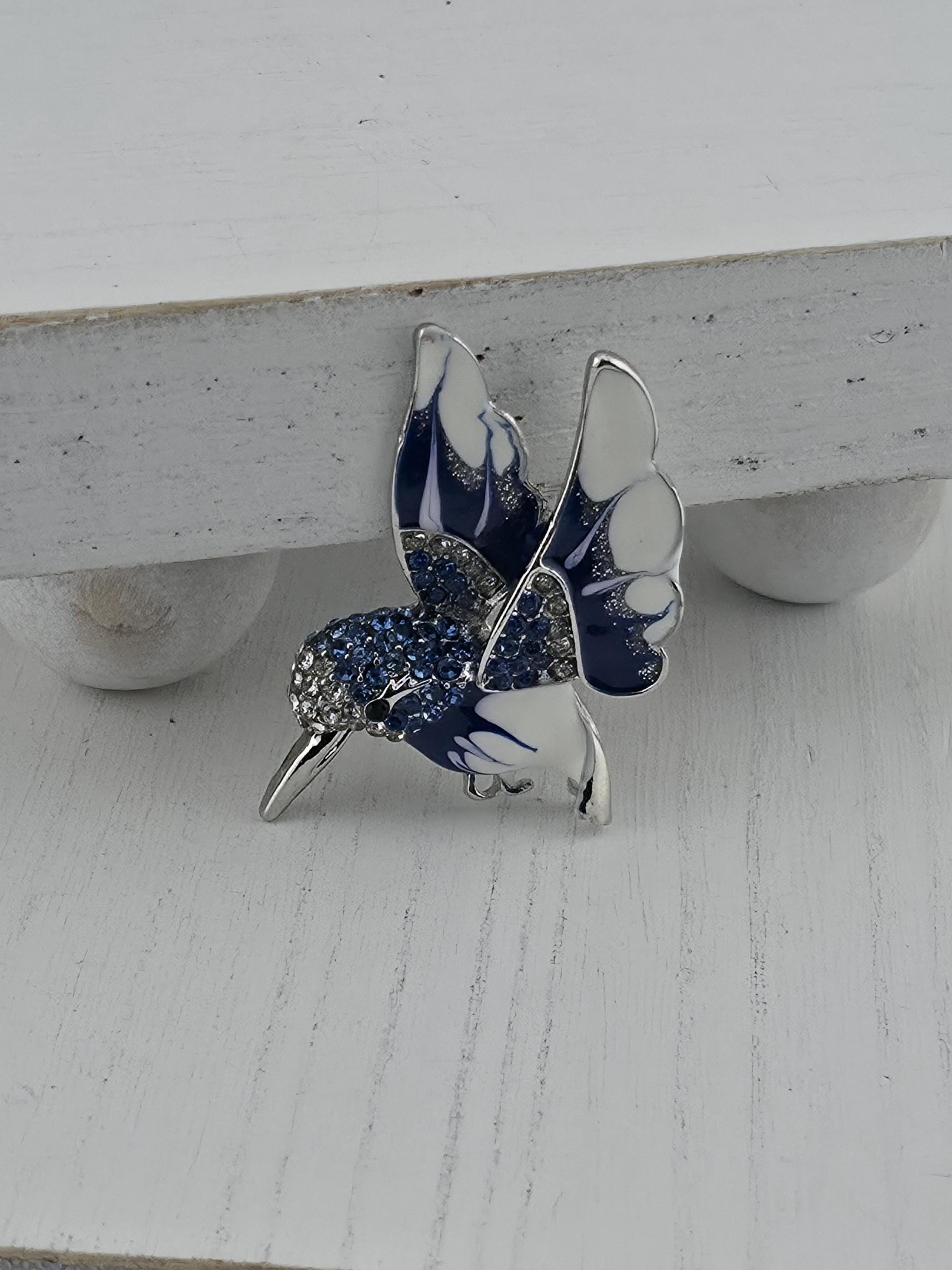 A silver and blue butterfly brooch with blue and white accents, including a blue and white butterfly wing and a blue and white body with blue and white accents.