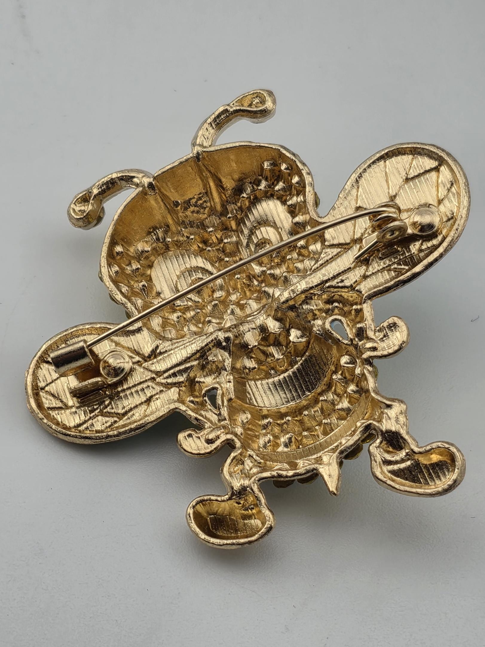 a gold-colored pin or brooch with an intricate, textured design.