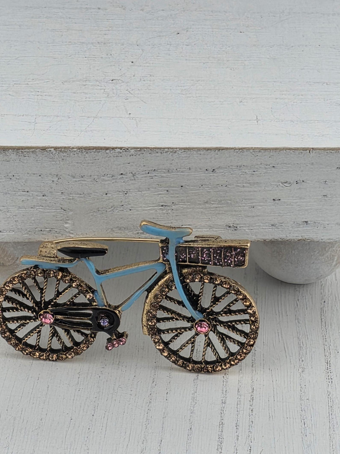 A decorative bicycle with a blue frame and gold accents, including rhinestones and a pink gemstone, is displayed in a white ornate frame.
