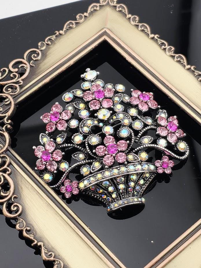 A decorative brooch with a floral design and sparkling rhinestones is displayed in a gold-framed picture frame.
