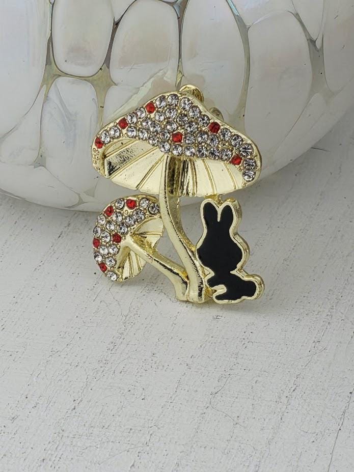 A decorative brooch in the shape of a mushroom with a small black rabbit figure on it, placed on a white surface.