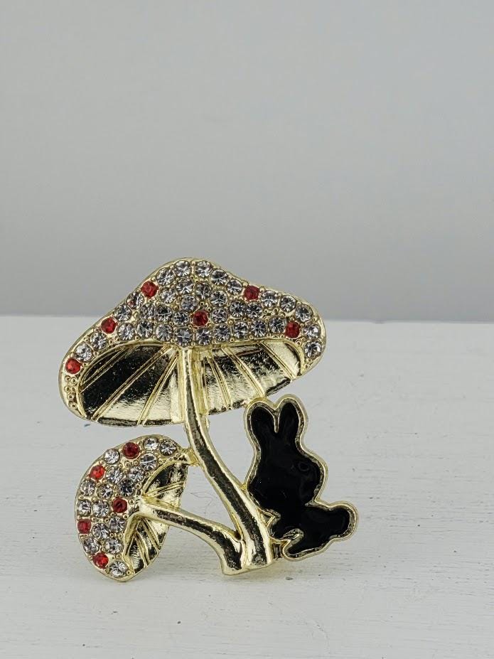 A decorative brooch in the shape of a mushroom with a black rabbit sitting on one of the mushroom's caps.