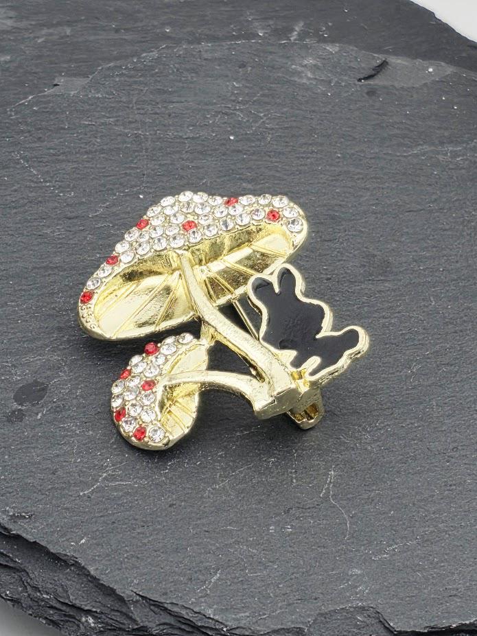 A gold-colored brooch with a mushroom-shaped design and red gemstones, placed on a gray surface.