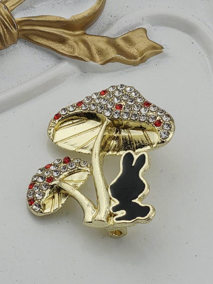 A decorative brooch featuring a golden mushroom with a black rabbit figure on it, set against a white background.