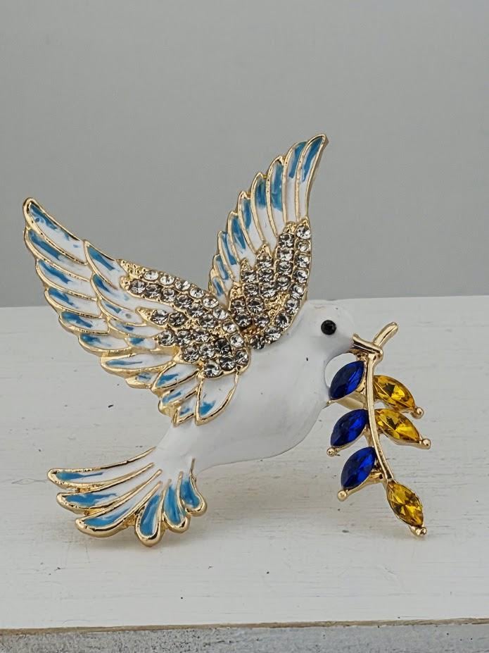 A decorative bird brooch with a white body, blue and gold accents, and a branch with blue and yellow gemstones.
